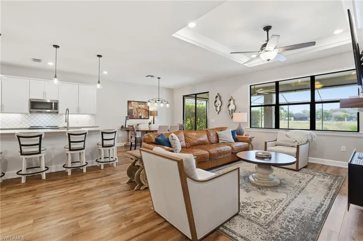 Living room featuring recessed lighting, light wood finished floors, a ceiling fan, a chandelier, and a raised ceiling