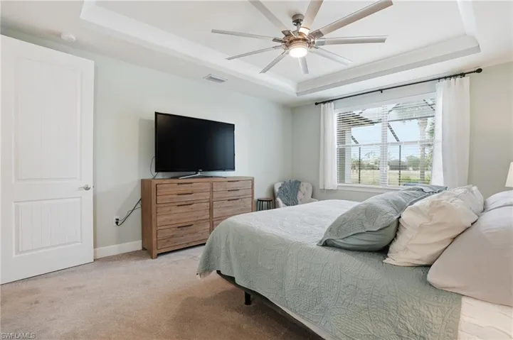 Bedroom with a tray ceiling, light carpet, and a ceiling fan