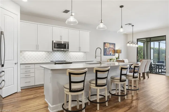 Kitchen featuring a kitchen island with sink, white cabinets, decorative light fixtures, and a breakfast bar area