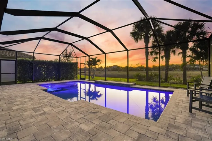 Pool at dusk featuring glass enclosure, an outdoor pool, a sunroom, and a patio area