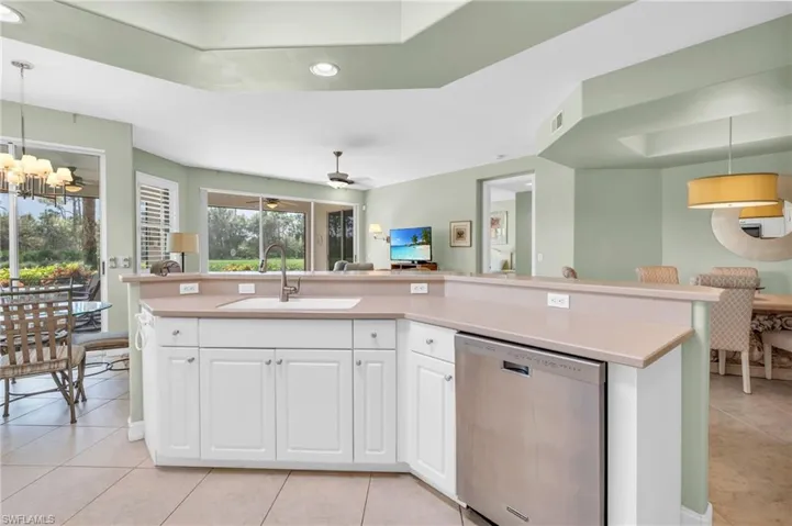Kitchen with stainless steel dishwasher, hanging light fixtures, ceiling fan with notable chandelier, and white cabinets