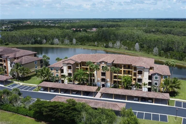 Lakeside condominium building featuring multi-story construction, covered parking, mature palm trees, and terracotta-style roof tiles