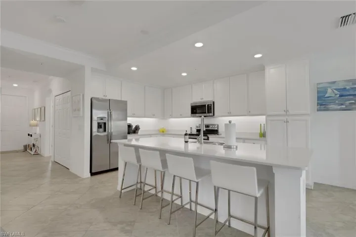 Modern kitchen featuring extensive white cabinetry, stainless steel appliances, and a large central island with seating