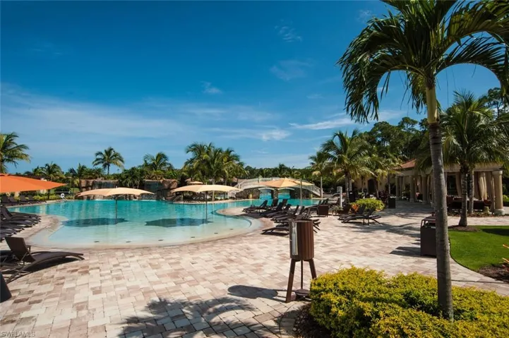 Expansive resort-style pool area featuring a freeform swimming pool with a beach entry, paver decking, multiple lounge chairs, and mature palm trees