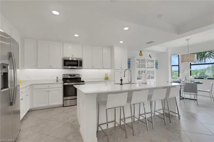 Modern kitchen featuring white cabinetry, stainless steel appliances, a center island with seating, a white solid surface countertop, and large format tile flooring