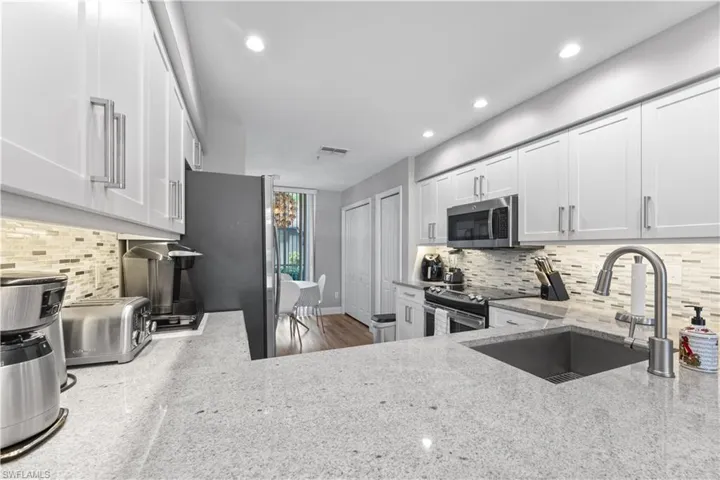 Kitchen featuring light stone counters, white cabinetry, stainless steel appliances, and tasteful backsplash
