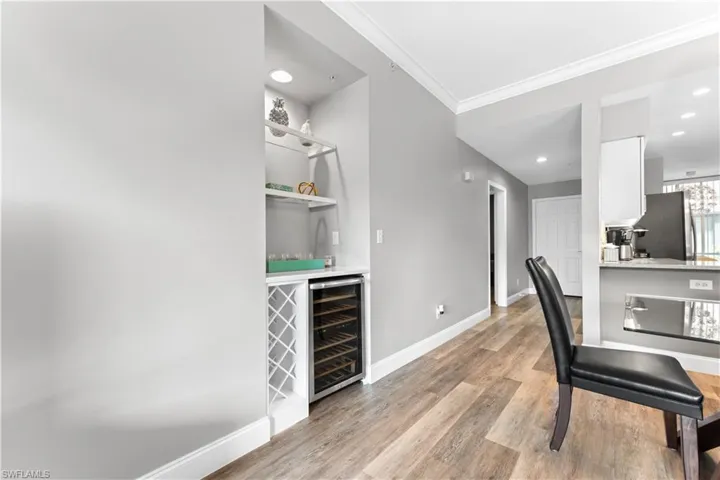 Office space with bar, light hardwood / wood-style floors, beverage cooler, and ornamental molding