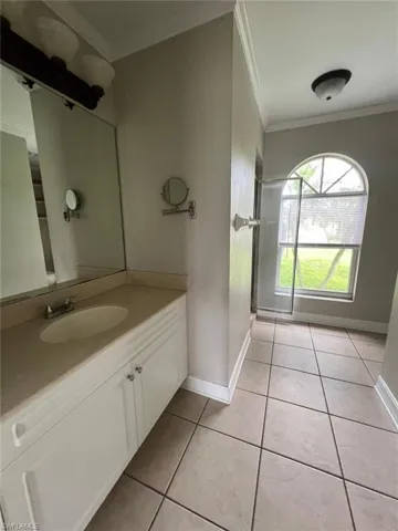 Bathroom with ornamental molding, vanity, light tile patterned flooring, and a stall shower