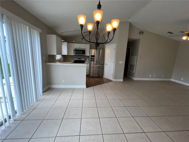 Kitchen with white cabinets, open floor plan, a chandelier, backsplash, and lofted ceiling