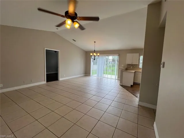 Empty room featuring light tile patterned flooring, a chandelier, ceiling fan, and vaulted ceiling