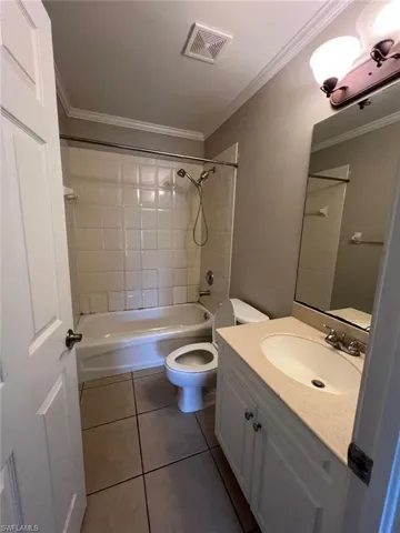 Bathroom featuring shower / tub combination, vanity, dark tile patterned flooring, and crown molding