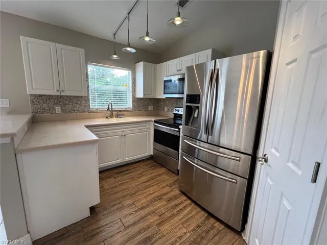 Kitchen with stainless steel appliances, light countertops, white cabinetry, and pendant lighting