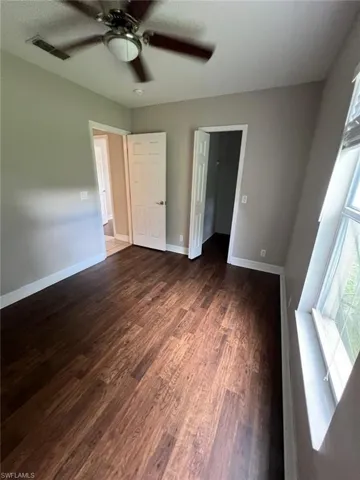 Unfurnished bedroom featuring a spacious closet, a textured ceiling, a ceiling fan, and dark wood-style floors