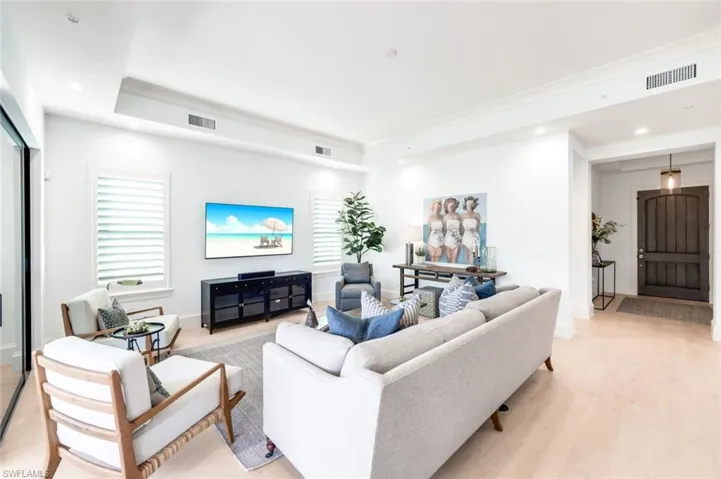 Living area with light wood finished floors, a tray ceiling, and recessed lighting