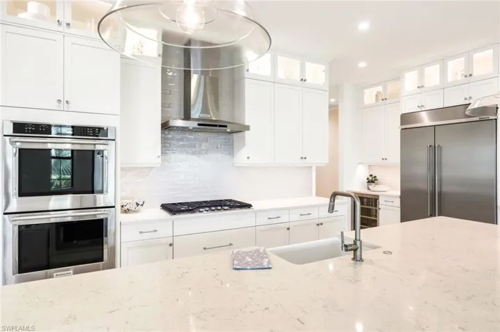 Kitchen with glass fronted cabinets, stainless steel appliances, white cabinets, decorative backsplash, and light stone counters