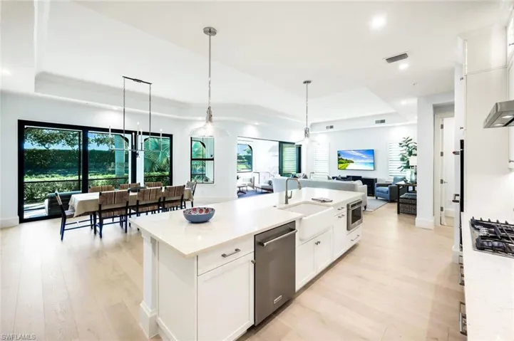 Kitchen with white cabinets, a tray ceiling, open floor plan, an island with sink, and light stone counters