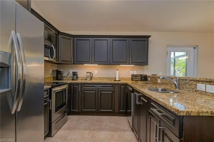 Kitchen featuring appliances with stainless steel finishes, light stone counters, backsplash, sink, and light tile floors