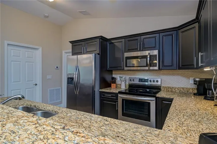 Kitchen with tasteful backsplash, light stone countertops, appliances with stainless steel finishes, sink, and lofted ceiling