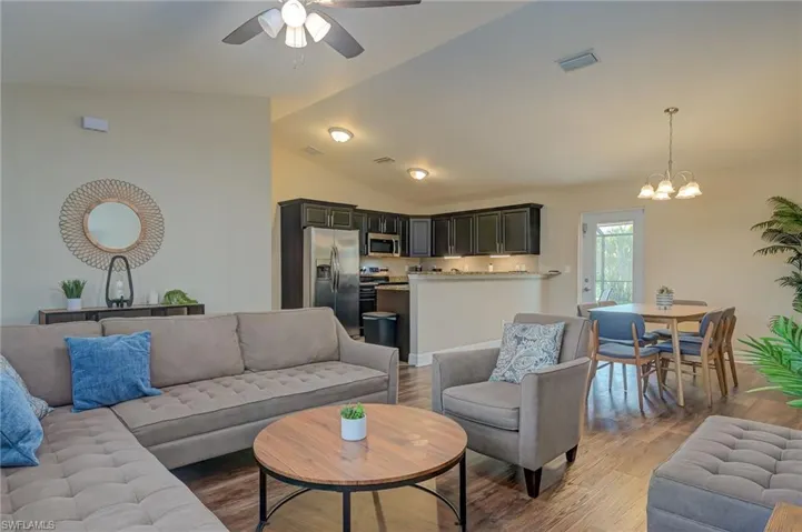 Living room featuring vaulted ceiling, hardwood / wood-style floors, and ceiling fan with notable chandelier