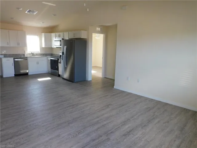 Kitchen featuring appliances with stainless steel finishes, white cabinetry, vaulted ceiling, dark wood-type flooring, and open floor plan