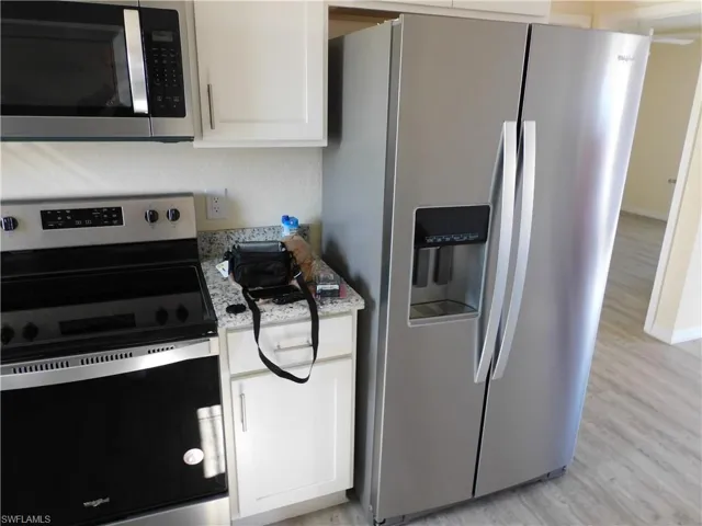 Kitchen with stainless steel appliances, white cabinetry, light wood-style floors, and light stone counters