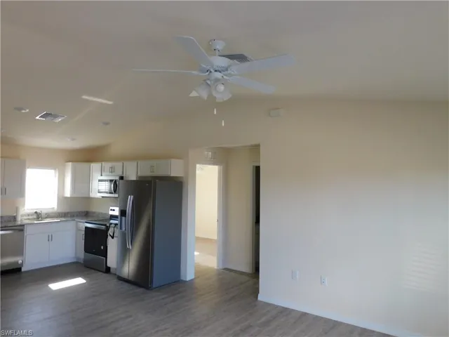 Kitchen featuring stainless steel appliances, white cabinets, dark wood-style floors, lofted ceiling, and a ceiling fan