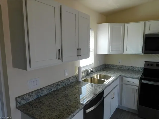 Kitchen with stainless steel appliances, light stone counters, and white cabinets