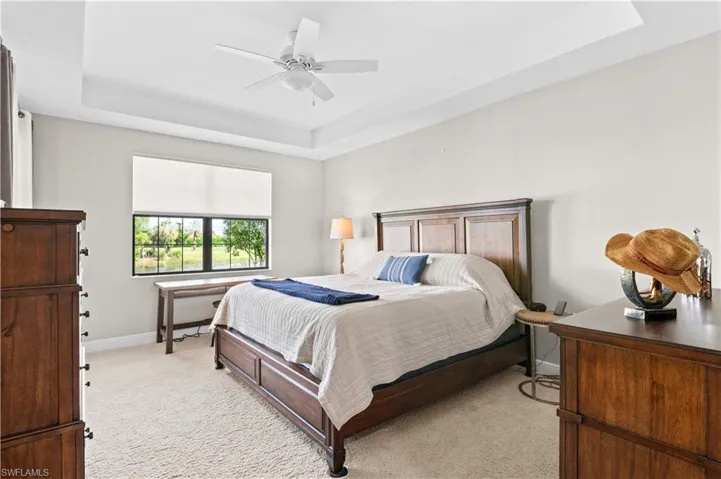 Bedroom featuring a raised ceiling, light colored carpet, and a ceiling fan