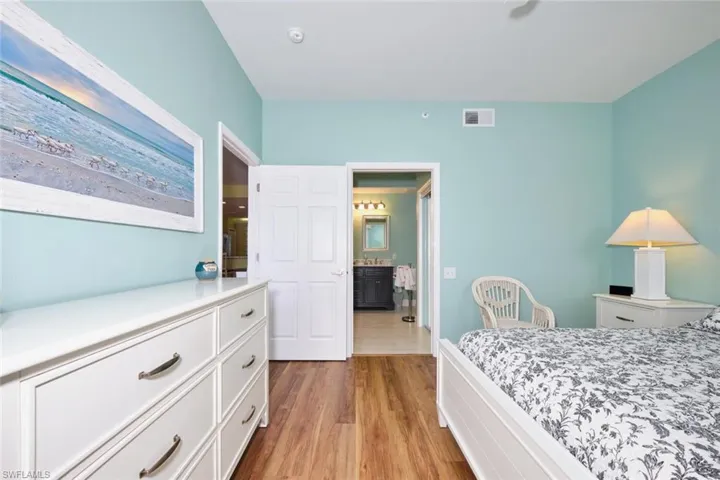 Bedroom featuring ensuite bathroom, visible vents, and wood finished floors
