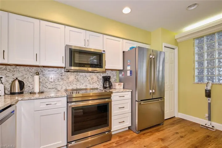 Kitchen with light stone countertops, appliances with stainless steel finishes, white cabinetry, light wood-type flooring, and backsplash