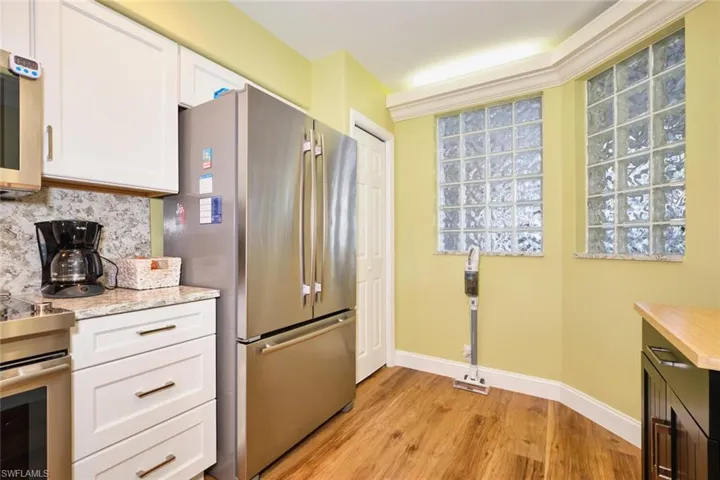 Kitchen with decorative backsplash, white cabinets, light wood finished floors, baseboards, and stainless steel appliances