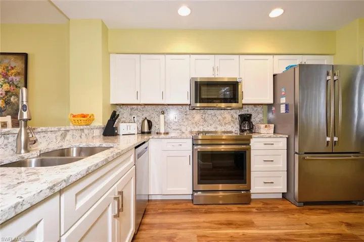 Kitchen featuring white cabinets, light stone countertops, appliances with stainless steel finishes, a sink, and light wood-type flooring