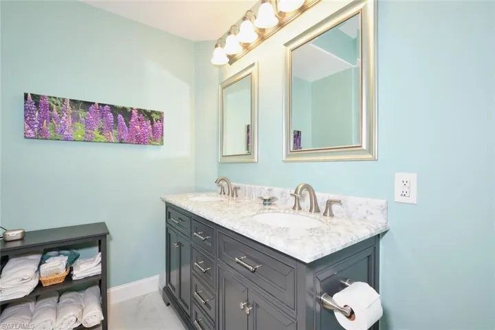 Full bath featuring baseboards, double vanity, a sink, and marble finish floor