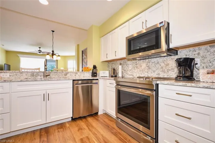 Kitchen featuring white cabinetry, stainless steel appliances, backsplash, a sink, and light wood-style flooring