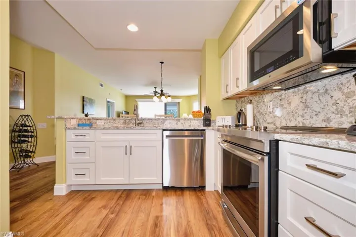 Kitchen with white cabinetry, tasteful backsplash, light wood-type flooring, a peninsula, and appliances with stainless steel finishes