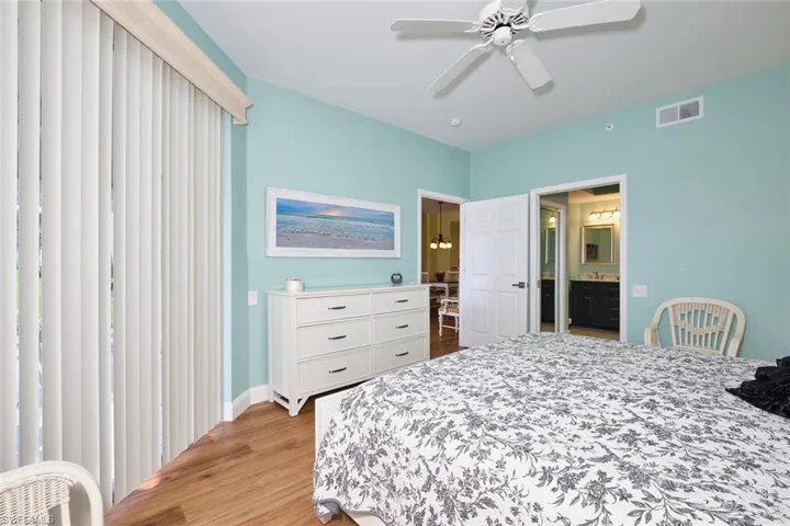 Bedroom with baseboards, ensuite bath, light wood-style floors, visible vents, and a ceiling fan