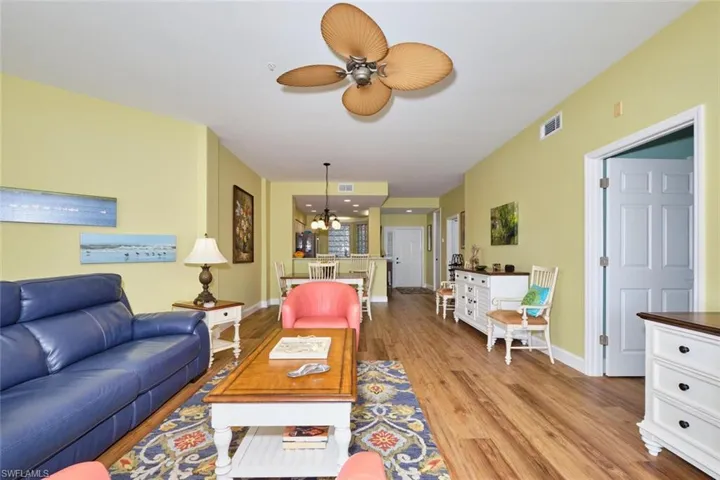 Living room featuring ceiling fan with notable chandelier, visible vents, light wood-style floors, and baseboards
