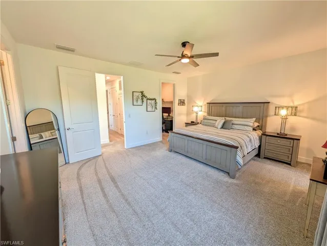 Bedroom with ensuite bathroom, light carpet, and ceiling fan