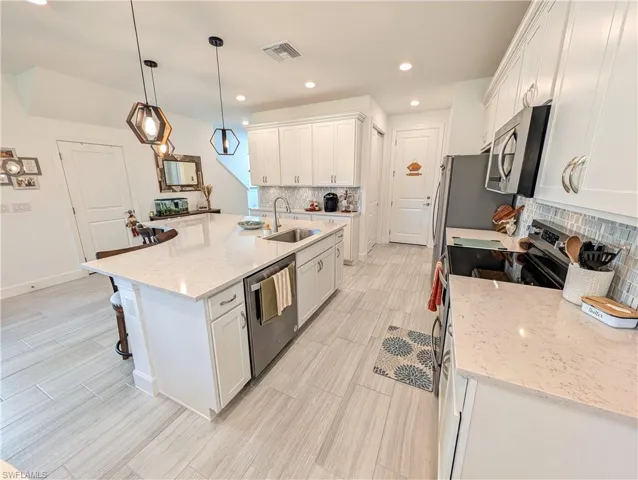 Kitchen with white cabinetry, appliances with stainless steel finishes, light stone counters, pendant lighting, and recessed lighting
