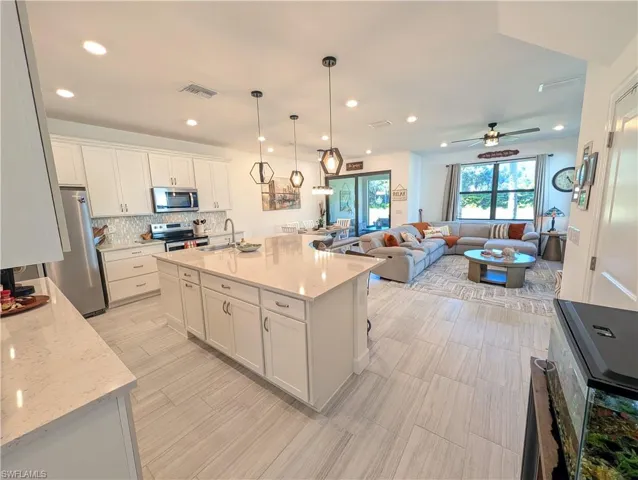 Kitchen featuring pendant lighting, light stone counters, white cabinets, tasteful backsplash, and open floor plan