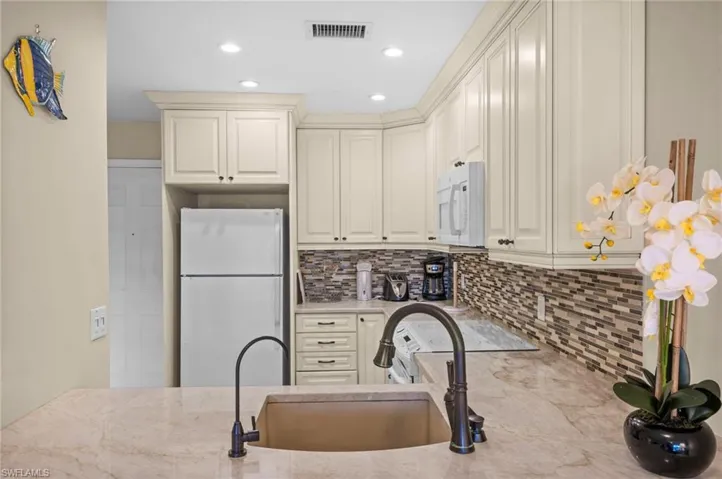 Kitchen with white appliances, light stone countertops, backsplash, recessed lighting, and cream cabinets