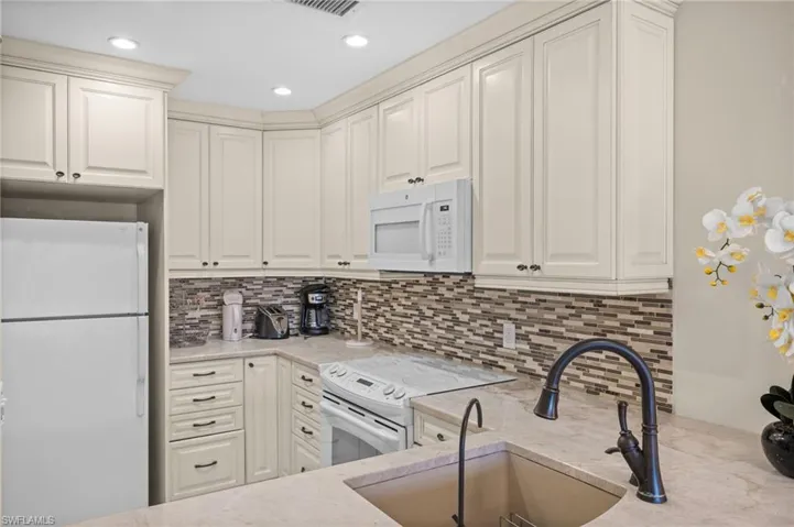 Kitchen with white appliances, light stone counters, decorative backsplash, recessed lighting, and white cabinets