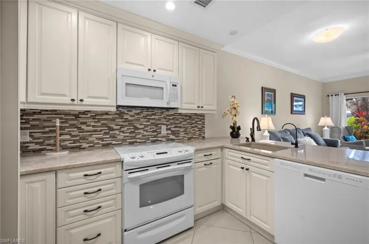 Kitchen featuring white appliances, light stone counters, open floor plan, crown molding, and light tile patterned floors