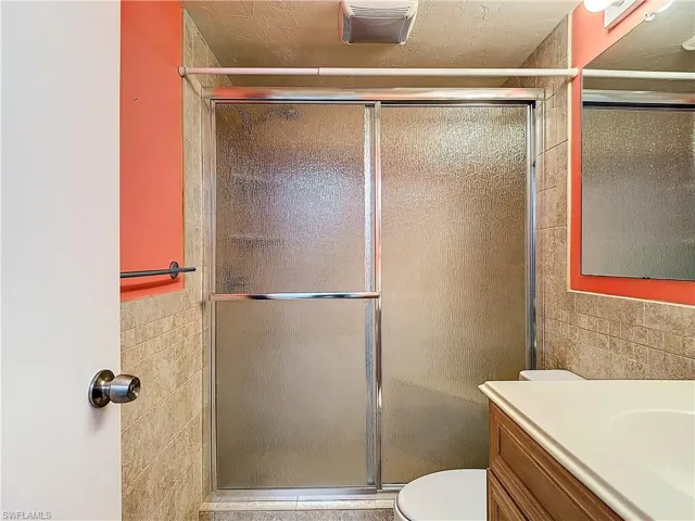 Bathroom with vanity, walk in shower, toilet, and tile walls