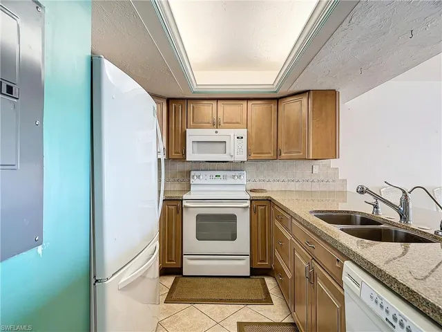Kitchen with light tile patterned flooring, tasteful backsplash, white appliances, sink, and a raised ceiling