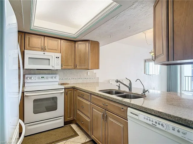 Kitchen featuring tasteful backsplash, a tray ceiling, white appliances, sink, and light tile patterned floors
