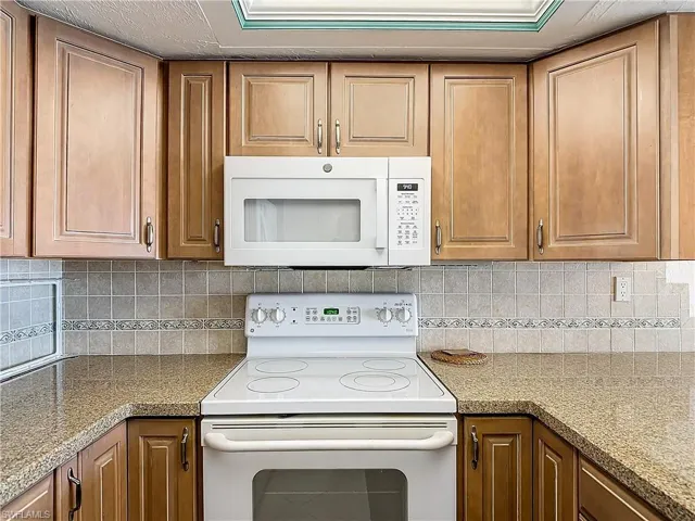 Kitchen with tasteful backsplash, light stone countertops, and white appliances