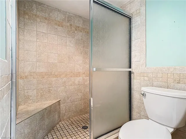 Bathroom with a shower with shower door, toilet, and tile walls