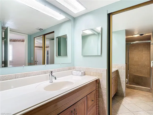 Bathroom with a shower with shower door, vanity, tile walls, and tile patterned floors