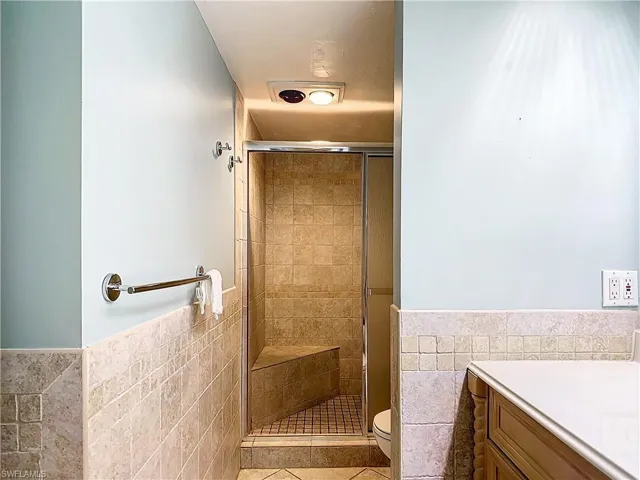 Bathroom with tile walls, a shower with shower door, toilet, and vanity